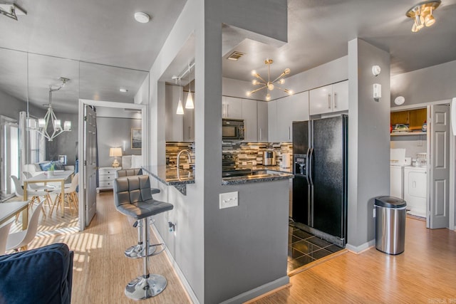 kitchen with an inviting chandelier, black fridge with ice dispenser, a peninsula, and washer and clothes dryer