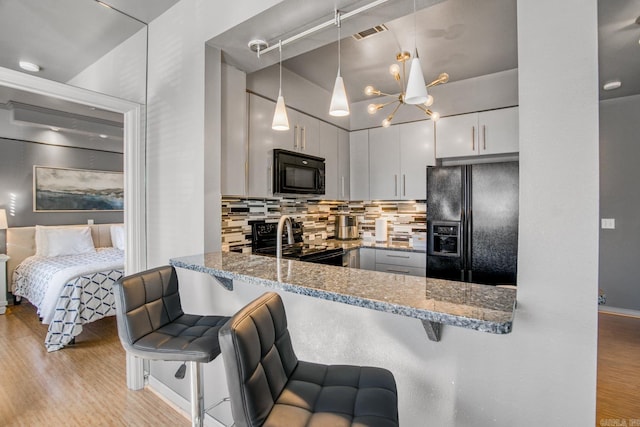 kitchen featuring a kitchen bar, black appliances, tasteful backsplash, wood finished floors, and light stone countertops