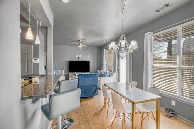 dining space with visible vents, plenty of natural light, ceiling fan with notable chandelier, and light wood-style floors