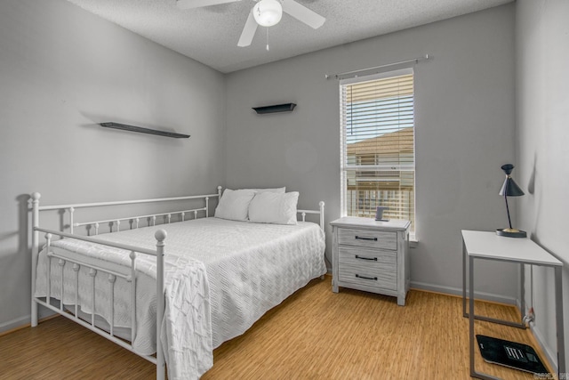 bedroom featuring baseboards, a textured ceiling, light wood-style floors, and a ceiling fan