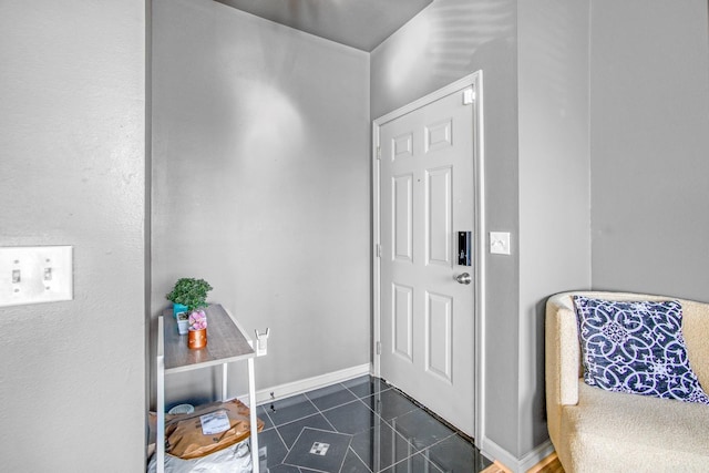 foyer with baseboards and dark tile patterned floors