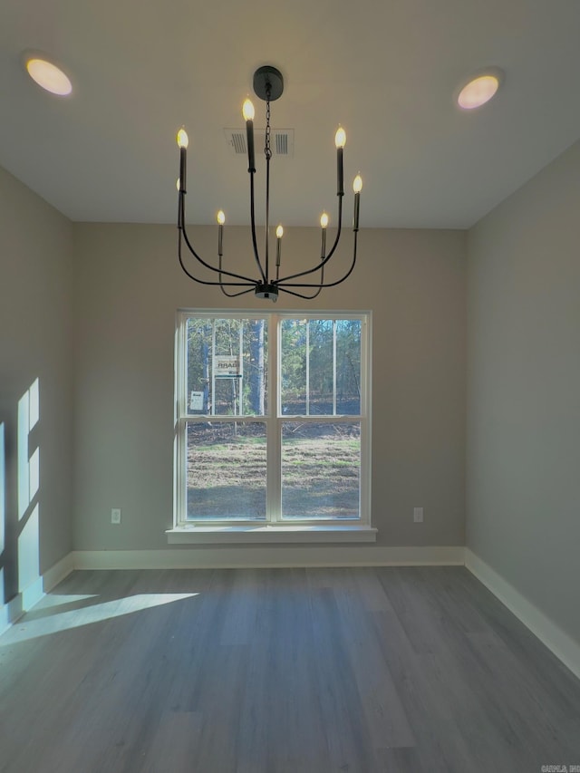 unfurnished dining area with baseboards, wood finished floors, visible vents, and a chandelier