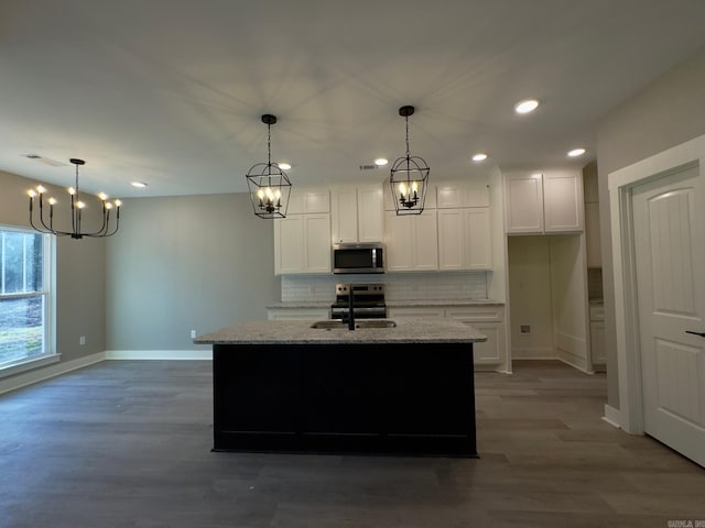 kitchen featuring wood finished floors, appliances with stainless steel finishes, white cabinets, decorative backsplash, and light stone countertops