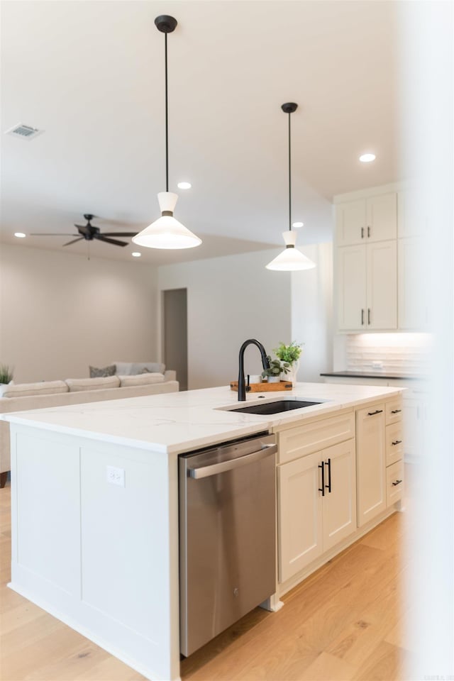 kitchen with light wood finished floors, a center island with sink, stainless steel dishwasher, white cabinetry, and a sink