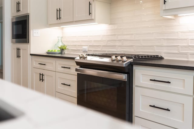 kitchen with dark countertops, backsplash, appliances with stainless steel finishes, and white cabinetry