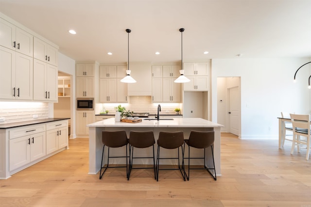 kitchen with white cabinets, built in microwave, light wood finished floors, and a sink