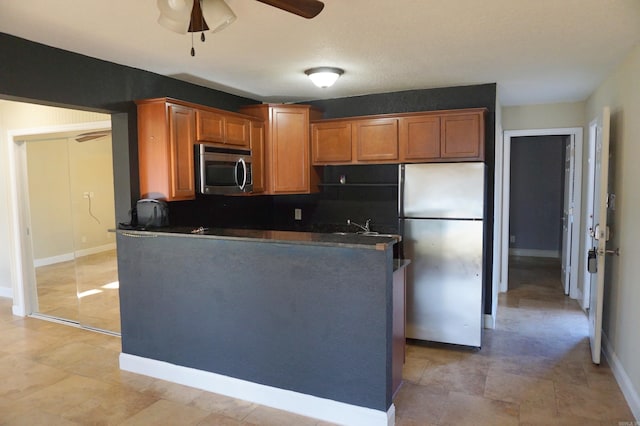 kitchen featuring baseboards, ceiling fan, stainless steel appliances, dark countertops, and brown cabinets