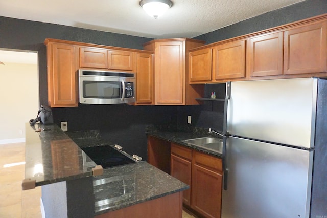 kitchen featuring appliances with stainless steel finishes, dark stone counters, a peninsula, and a sink