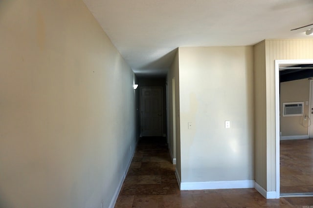 corridor with stone finish flooring, baseboards, and a wall unit AC