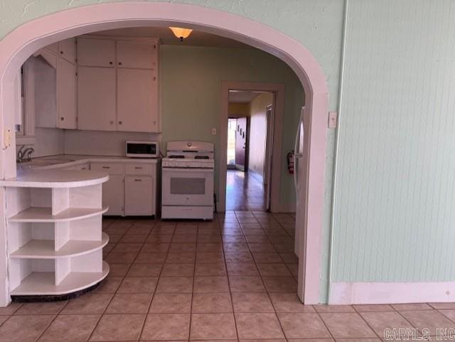 kitchen featuring open shelves, gas range gas stove, white cabinetry, light countertops, and light tile patterned floors