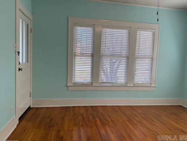 unfurnished room with a wealth of natural light, baseboards, wood finished floors, and ornamental molding