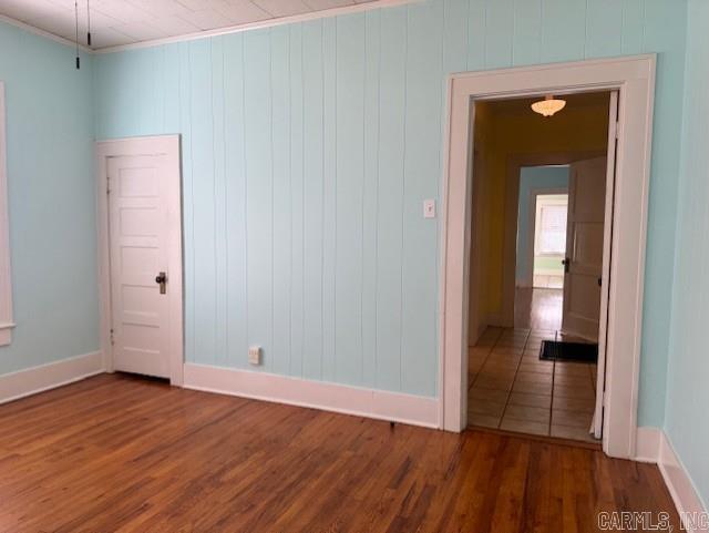 empty room with baseboards, wood finished floors, and crown molding