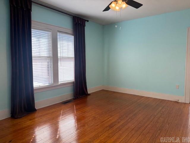 unfurnished room with ceiling fan, visible vents, baseboards, and wood finished floors