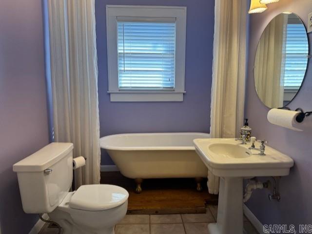 full bath with tile patterned floors, a soaking tub, and toilet