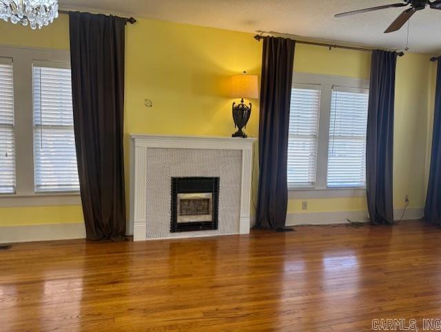 unfurnished living room with plenty of natural light, ceiling fan with notable chandelier, a fireplace, and wood finished floors