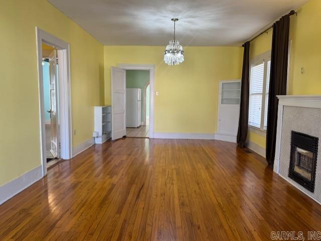 unfurnished living room with a chandelier, baseboards, wood finished floors, and a tile fireplace