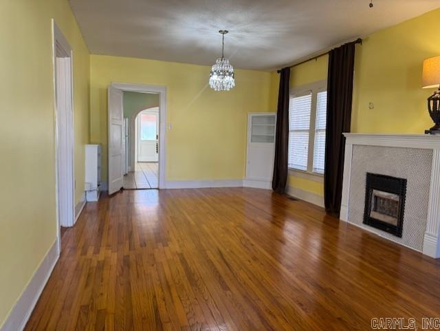 unfurnished living room with a chandelier, plenty of natural light, a fireplace, and wood finished floors