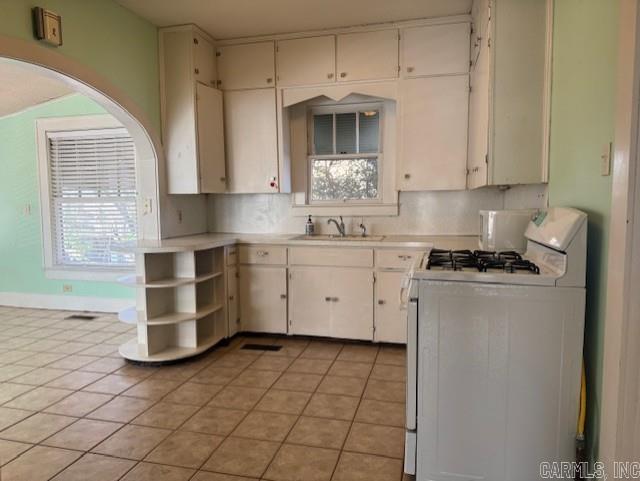 kitchen with open shelves, tasteful backsplash, light tile patterned flooring, light countertops, and white range with gas stovetop