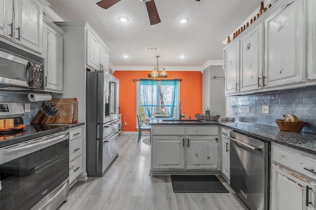 kitchen with visible vents, light wood finished floors, a peninsula, ornamental molding, and stainless steel appliances