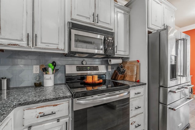 kitchen featuring dark stone counters, stainless steel appliances, white cabinetry, crown molding, and backsplash