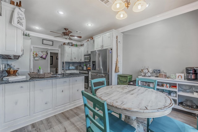 kitchen with dark stone countertops, a peninsula, a sink, appliances with stainless steel finishes, and crown molding