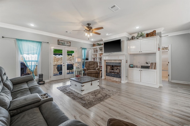 living area with light wood-type flooring, visible vents, a tiled fireplace, french doors, and crown molding