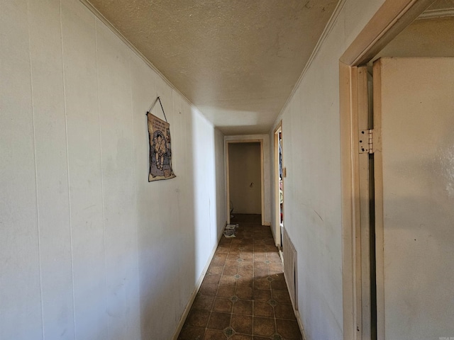 corridor featuring dark tile patterned floors, a textured ceiling, and crown molding