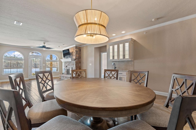 dining room featuring a stone fireplace, crown molding, wood finished floors, and visible vents