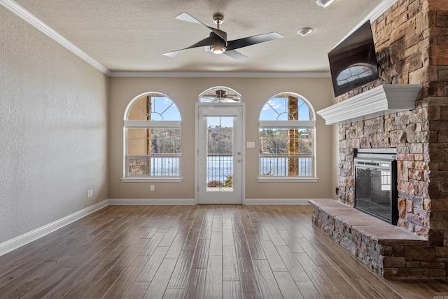 unfurnished living room featuring a stone fireplace, a textured ceiling, wood finished floors, and ornamental molding