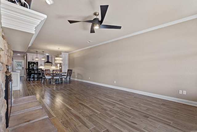 interior space with a ceiling fan, baseboards, a fireplace, dark wood-style flooring, and crown molding