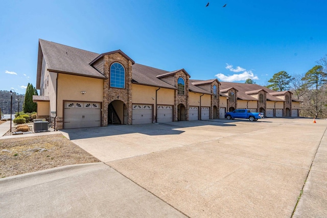 view of front of house with stone siding, stucco siding, central air condition unit, and concrete driveway