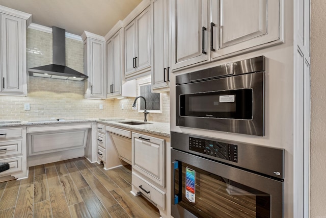 kitchen featuring decorative backsplash, appliances with stainless steel finishes, wall chimney exhaust hood, and a sink