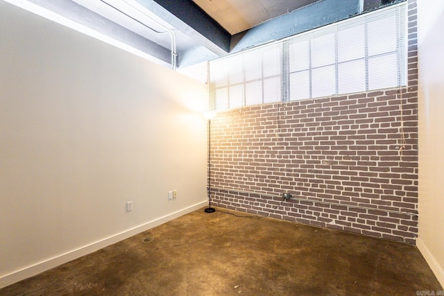 empty room with baseboards, concrete flooring, and brick wall