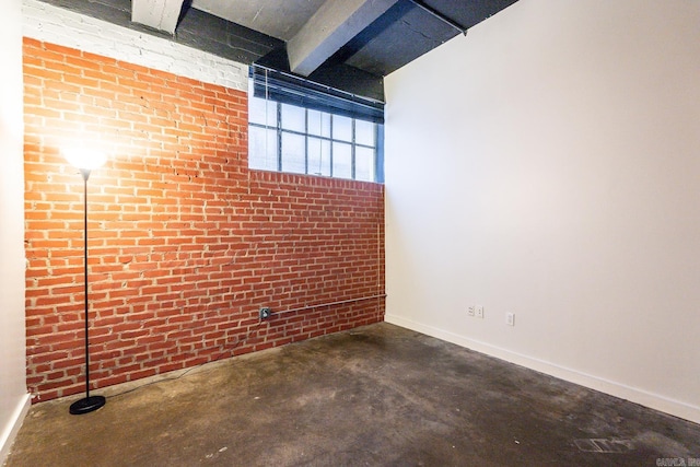 empty room with beamed ceiling, unfinished concrete floors, and brick wall