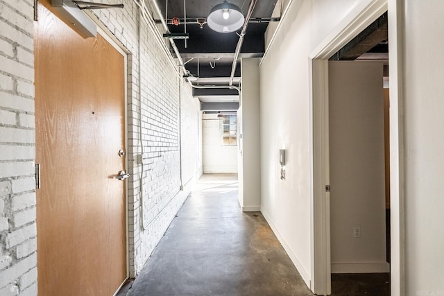 hall with baseboards, concrete flooring, and brick wall