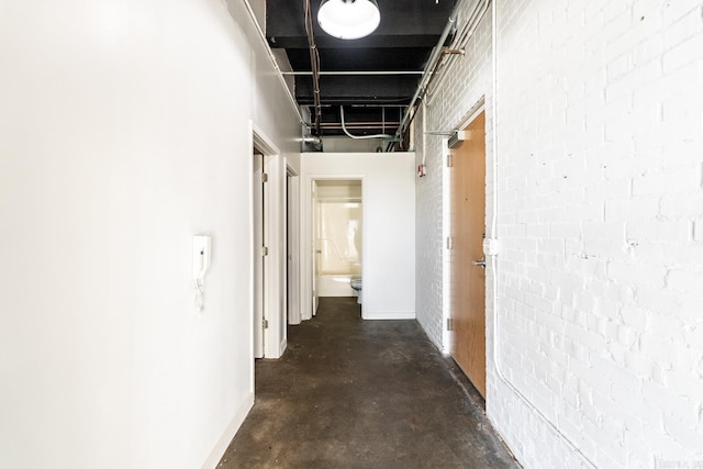 corridor with brick wall and unfinished concrete flooring