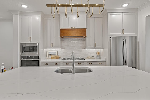 kitchen featuring light stone counters, a sink, appliances with stainless steel finishes, white cabinetry, and backsplash