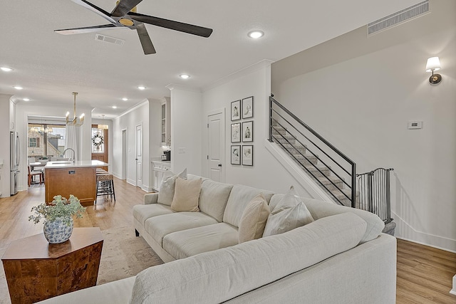 living area featuring stairway, ornamental molding, visible vents, and light wood-type flooring