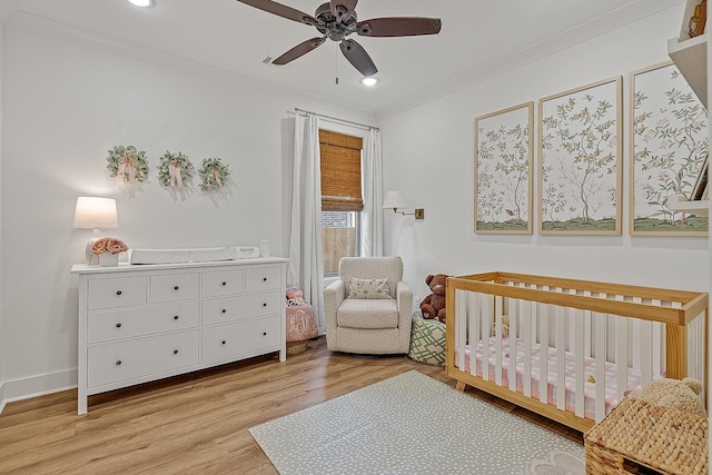 bedroom with baseboards, light wood-style flooring, recessed lighting, ornamental molding, and a crib