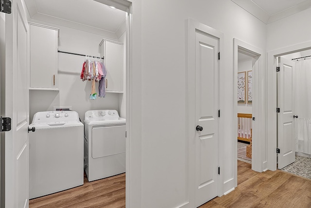 clothes washing area with cabinet space, washing machine and dryer, light wood-type flooring, and ornamental molding