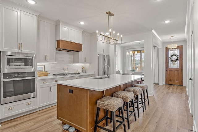 kitchen featuring an island with sink, a sink, appliances with stainless steel finishes, an inviting chandelier, and light countertops