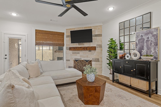 living area with visible vents, ornamental molding, a ceiling fan, wood finished floors, and a stone fireplace