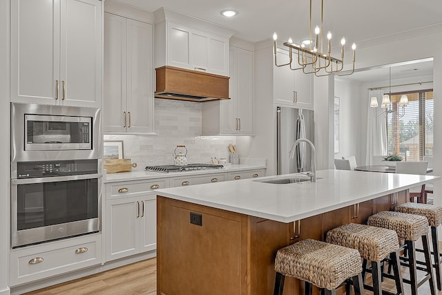 kitchen with custom exhaust hood, a sink, appliances with stainless steel finishes, a notable chandelier, and backsplash