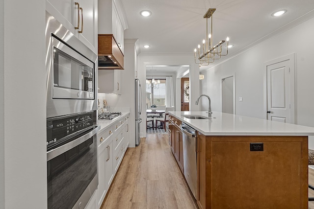 kitchen with brown cabinetry, a center island with sink, ornamental molding, a sink, and appliances with stainless steel finishes