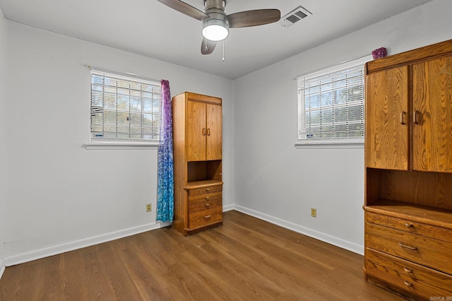 unfurnished bedroom featuring visible vents, baseboards, multiple windows, and wood finished floors