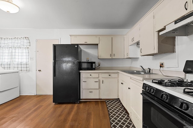 kitchen featuring under cabinet range hood, dark wood finished floors, washer / dryer, black appliances, and a sink