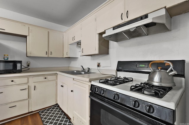 kitchen featuring black microwave, under cabinet range hood, light countertops, range with gas stovetop, and a sink