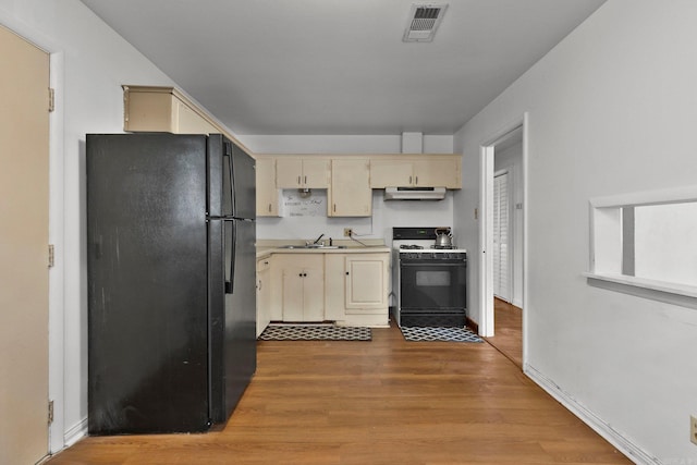 kitchen featuring under cabinet range hood, cream cabinets, wood finished floors, gas range oven, and freestanding refrigerator