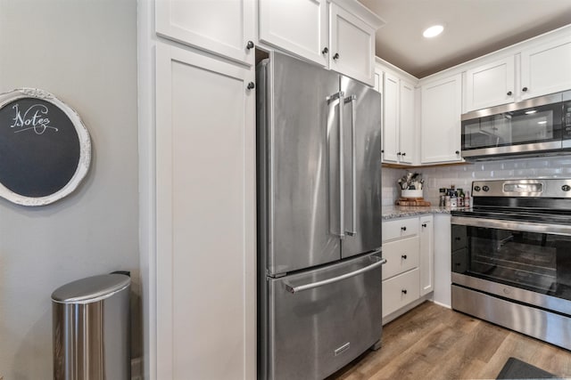 kitchen with tasteful backsplash, light stone counters, appliances with stainless steel finishes, wood finished floors, and white cabinets