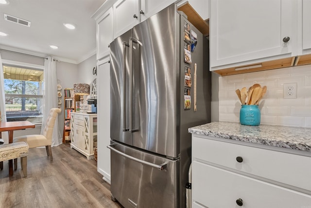 kitchen with wood finished floors, visible vents, freestanding refrigerator, white cabinets, and backsplash